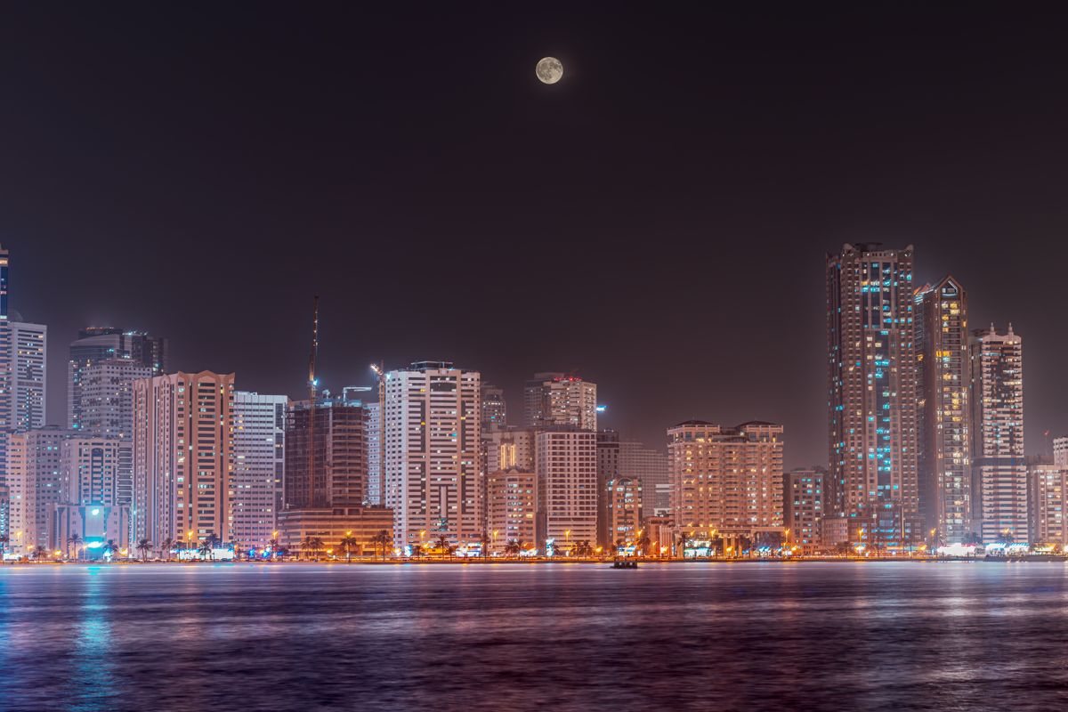 Sharjah waterfront skyline at night under a full moon