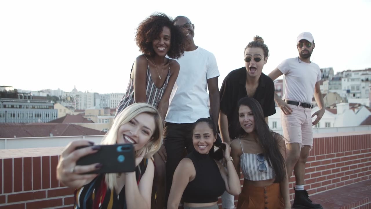 A group of friends laughing together while taking a selfie on a rooftop at golden hour